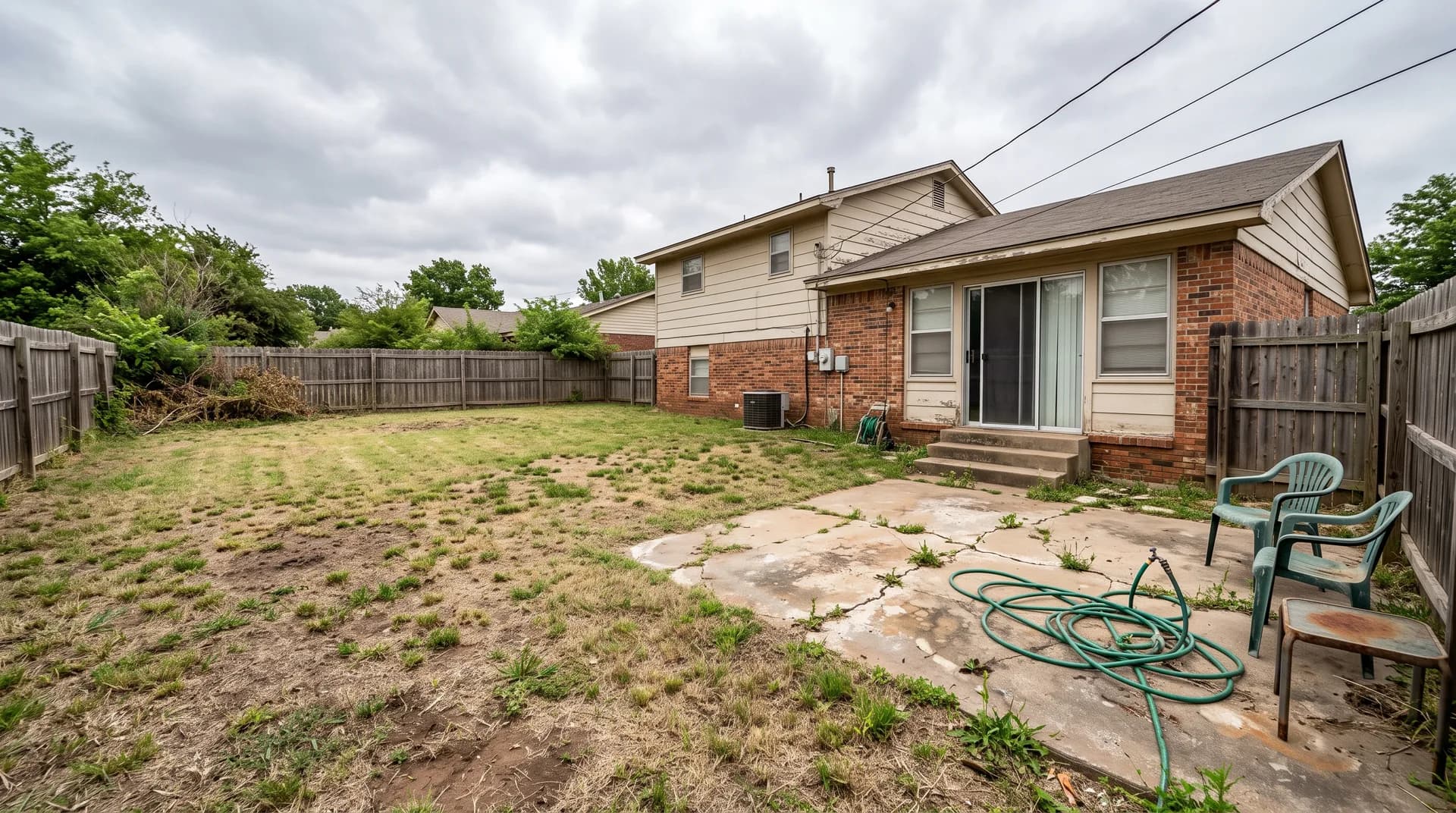 Bare backyard with patchy dry lawn and a cracked concrete patio before renovation